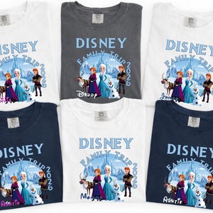 Może przedstawiać: R&oacute;żne koszulki z motywem Disney Family Trip 2026. Koszulki są dostępne w kolorze białym, szarym i granatowym. Projekt zawiera postacie z filmu Kraina Lodu. Niekt&oacute;re koszulki mają nadrukowane imiona.