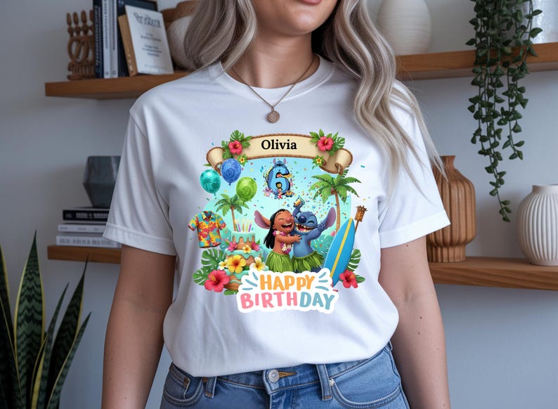 May include: White t-shirt featuring a colorful graphic with the text "Olivia" and "Happy Birthday." The design includes cartoon characters, palm trees, balloons, and a surfboard. The number 6 is also visible in the design.