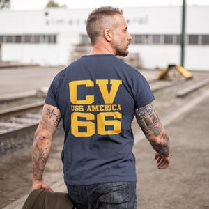 May include: A navy blue t-shirt with a yellow graphic on the back. The graphic says "CV USS AMERICA 66".