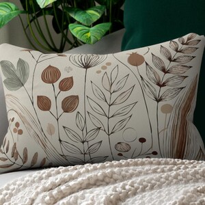 May include: A beige throw pillow with a floral pattern in brown and green hues. The pillow is on a white couch with a green throw blanket.