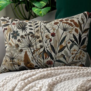 Whimsical Botanical Lumbar Pillow. Featuring various flowers, leaves, and branches in earthy tones with pops of deep red and mustard yellow.