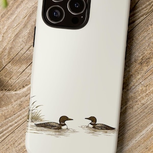 May include: A white phone case featuring an illustration of two loons swimming in water. The loons are brown and black with white accents. The case has a glossy finish and a camera cutout.