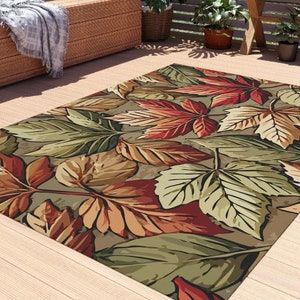 May include: A colorful outdoor rug with a leafy pattern in shades of green, brown, red, and orange. The rug is made of durable material and is perfect for adding a touch of nature to any outdoor space.
