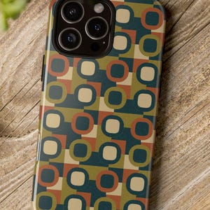 以下が含まれることがあります： レトロな幾何学模様のスマートフォンケース。ティール、ブラウン、ベージュ、オレンジの色合い。光沢のある仕上がりで、カメラの切り抜きがあります。木製の表面にケースが置かれています。