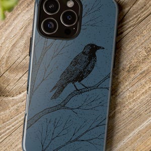 May include: A dark blue phone case featuring a black crow perched on a tree branch. The crow and branches are illustrated in black against a textured background. The case has a glossy finish and a camera cutout.