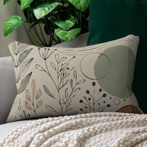 May include: A beige throw pillow with a floral pattern in shades of green, brown, and beige. The pillow is on a white couch with a green throw blanket.