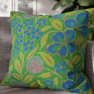 Könnte beinhalten: Ein grünes Kissen mit einem Blumenmuster mit blauen, gelben und rosa Blüten. Das Kissen ist aus einem weichen, bequemen Stoff gefertigt und perfekt, um jedem Raum einen Hauch von Farbe und Stil zu verleihen.