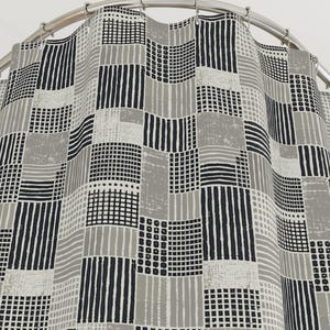 May include: A shower curtain featuring a patchwork pattern of black, white, and gray squares. Each square contains distinct geometric designs, including vertical stripes, horizontal lines, and grids, suspended from a curved metal shower rod.