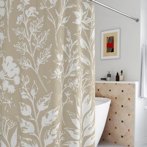 Könnte beinhalten: Ein beiger Duschvorhang mit einem weißen Blumenmuster. Der Duschvorhang hängt in einem Badezimmer mit einer weißen Badewanne und einer weißen gekachelten Wand.