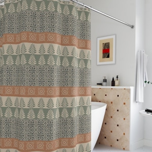Może przedstawiać: Wzorzysta zasłona prysznicowa z powtarzającym się wzorem liści, kształtów geometrycznych i pasków w odcieniach zieleni, beżu i brązu. Zasłona wisi na zakrzywionym, srebrnym drążku prysznicowym. Łazienka ma białą wannę i ściany.