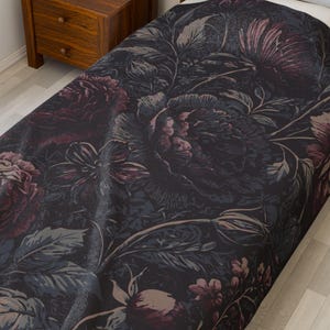 May include: A dark gray throw blanket with a floral pattern featuring large pink roses and leaves. The blanket is made of a soft, textured fabric.