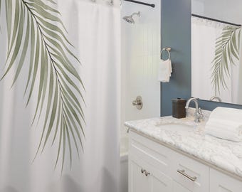 Pode incluir: Cortina de duche branca com uma grande folha de palmeira em estilo aquarela em tons de verde. A casa de banho tem armários brancos, uma bancada de mármore e um chão de azulejos cinza escuro. Um espelho reflete a cortina.