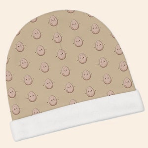 May include: A tan baby beanie with a white brim. The beanie has a repeating pattern of brown potatoes with smiling faces.