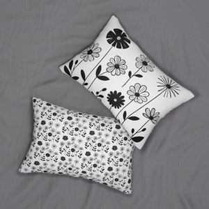 Op de afbeelding: Twee witte kussenslopen met zwarte bloemenpatronen. Een kussensloop heeft een herhalend patroon van kleine bloemen en de andere heeft een groter bloemenpatroon met stelen.