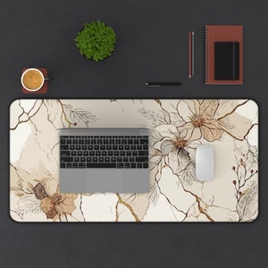 Op de afbeelding: Een witte bureauonderlegger met een bloemenpatroon met bruine en gouden bloemen en bladeren. Een laptop en een witte muis liggen op de bureauonderlegger.