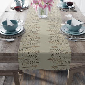 May include: A beige table runner with a floral pattern featuring brown and gold leaves and flowers. The runner is on a wooden table with two place settings on each side.