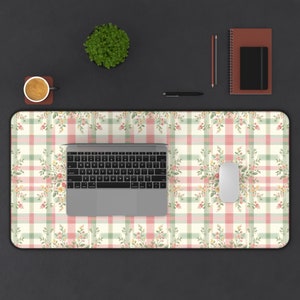 May include: A floral and plaid patterned desk mat in cream, pink, and green, with a laptop, mouse, and other office supplies. The mat features a repeating pattern of flowers and a plaid design. A cup of coffee, a plant, and a notebook are also visible.