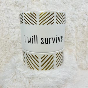 May include: White ceramic planter with a gold geometric pattern and the text "i will survive."