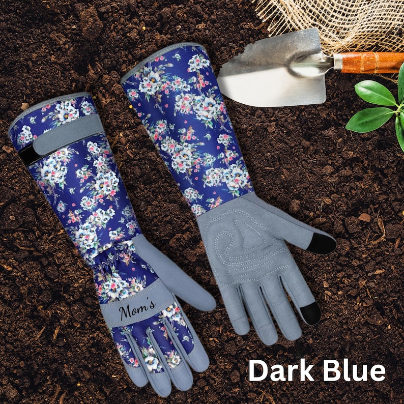 Peut inclure: Gants de jardinage bleu fonc&eacute; avec un motif floral et des paumes grises. Les gants ont de longs poignets et le mot "Mom's" est imprim&eacute; sur l'un des gants. Une petite truelle de jardin est en arri&egrave;re-plan.