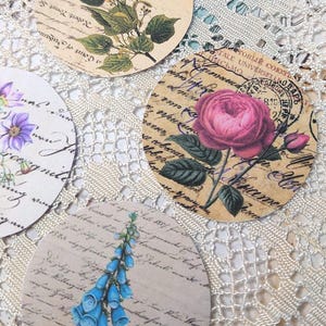 以下が含まれることがあります： 花や葉の植物画が描かれた丸い紙の切り抜きコレクション。各切り抜きは、手書きのスクリプトの背景と、ピンク、青、緑の色合いのさまざまな花のモチーフを備えたヴィンテージの美学を持っています。