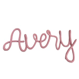 以下が含まれることがあります： ピンク色の筆記体で書かれた「Avery」という単語。太い編み物素材でできています。文字はつながっており、柔らかく丸みを帯びた外観です。背景は無地の白です。
