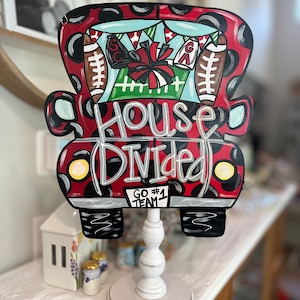 May include: A red and black truck cutout with a white base. The truck has black polka dots and the words "House Divided" written on the front. The truck has a cheerleader pom pom and footballs in the back. The text "Go #1 Team" is written on the bottom of the truck.