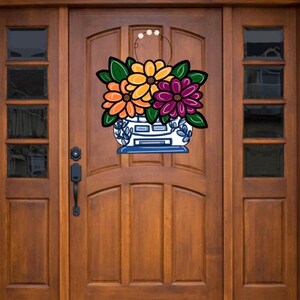May include: A blue and white ceramic planter with a floral design. The planter is filled with orange, yellow, and purple flowers. The planter is hanging on a wooden door.