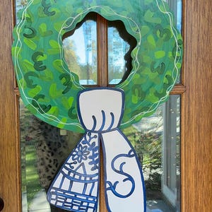 May include: A green wreath with a white outline and a white bow with blue details. The bow is tied in a knot and has a floral pattern.