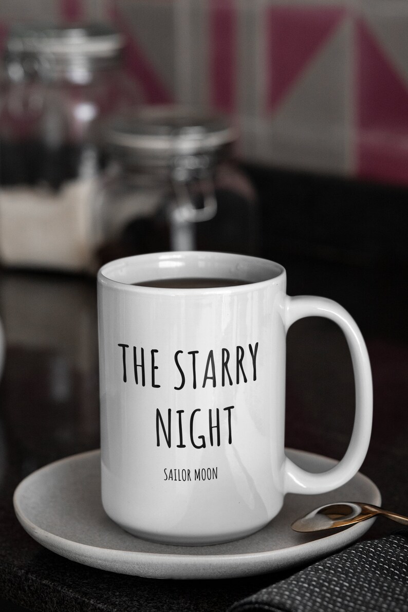 May include: White ceramic coffee mug with black text that reads "The Starry Night Sailor Moon". The mug is sitting on a white saucer.