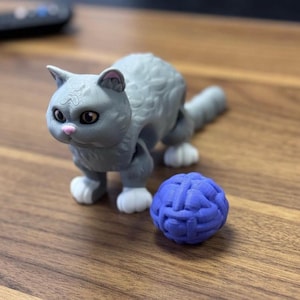 May include: A gray and white toy cat with a pink nose and blue eyes, playing with a blue yarn ball.