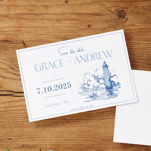 May include: Save the date cards with a lighthouse illustration in blue ink. The cards feature the names "Grace + Andrew" and the date "7.10.2025". A blank card is next to the save the date card on a wooden surface.