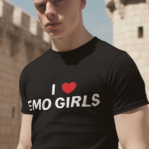 Puede incluir: Un hombre con una camiseta negra con el texto "I ♥ EMO GIRLS" en blanco. Lleva pantalones rojos y tiene el pelo corto y rubio.