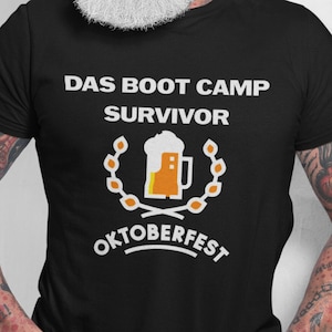 May include: Black t-shirt with white text that reads "Das Boot Camp Survivor Oktoberfest". The text is surrounded by a wreath with a beer stein in the centre.