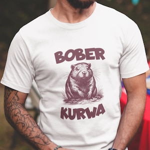 Op de afbeelding: Wit T-shirt met een bruine bever afbeelding en de tekst "BOBER KURWA" in bruin.