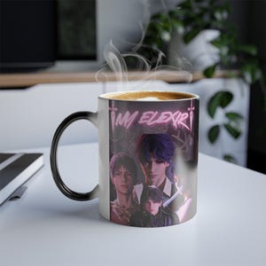 May include: A white ceramic mug with a black handle, featuring a colour-changing design. The mug displays the text "MM ELIXIR" in pink neon, along with an illustration of anime characters. Steam rises from the coffee inside.
