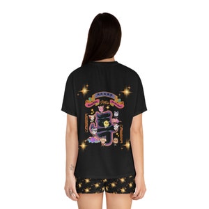 Peut inclure: Ensemble pyjama noir avec un t-shirt à manches courtes orné d'un motif d'animaux de dessin animé et du texte "Stray Kids" et "The 5-Star Album". Le short de pyjama est noir avec des étoiles dorées.