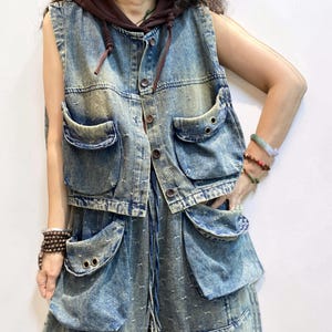 May include: A denim vest with a brown hood and matching denim pants. The vest has multiple large pockets and button closures. The denim is a faded blue with a distressed look. The pants also have large pockets.