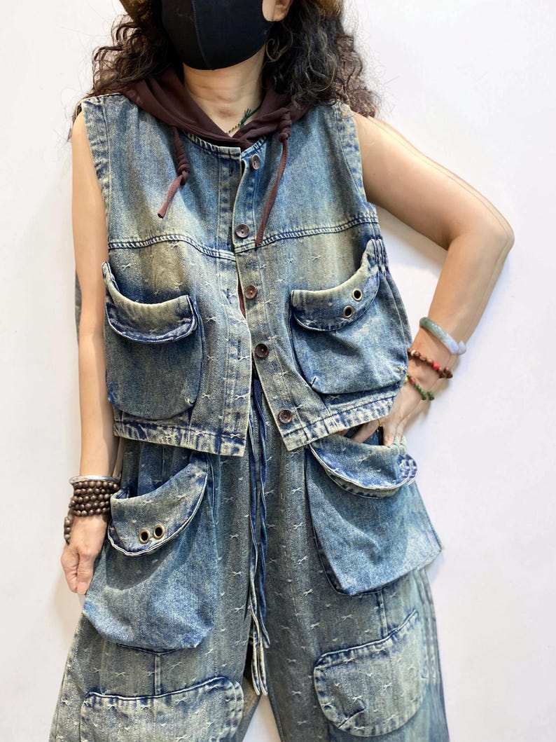 May include: A denim vest with a brown hood and matching denim pants. The vest has multiple large pockets and button closures. The denim is a faded blue with a distressed look. The pants also have large pockets.
