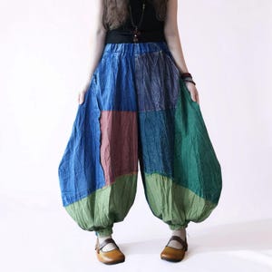 Könnte beinhalten: Weit geschnittene Hose mit Patchwork-Design aus großen blauen, dunkelroten und grünen Stoffbahnen. Die Hose verfügt über einen elastischen Bund, eine voluminöse Silhouette, die an den Knöcheln mit elastischen Bündchen abschließt, und sichtbare Nähte.