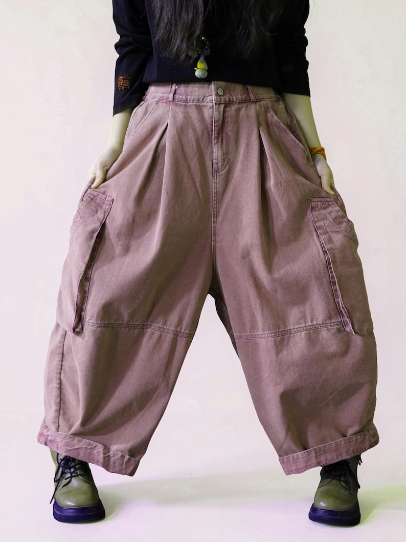 May include: Dusty rose wide-leg cargo pants featuring a high-waisted design with front pleats, two large side cargo pockets, and a button-fly closure. The pants have a loose, voluminous silhouette with cuffed hems and visible stitching details.