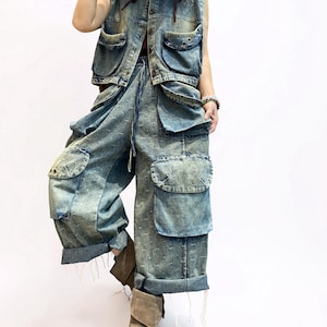 May include: A denim vest and matching cargo pants set in a light blue wash. The vest has multiple pockets and a drawstring. The pants feature oversized pockets and a relaxed fit. The outfit is paired with brown boots.