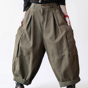 May include: Olive green wide-leg cargo pants featuring a high-waisted design with front pleats, large side utility pockets, and a cuffed hem. The pants have a button and zipper closure at the waist and a loose, voluminous silhouette throughout the legs.