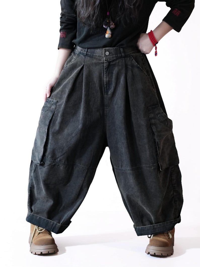 May include: Charcoal gray denim cargo pants featuring a high-waisted design with front pleats, large side utility pockets, and a loose, wide-leg silhouette that tapers slightly at the hem. The pants have a button closure and visible stitching.