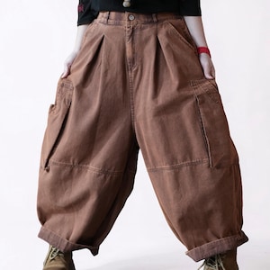 May include: Brown cargo pants featuring a high-waisted design with front pleats, a button closure, and large side pockets. These wide-leg trousers have a loose, voluminous fit with cuffed hems, providing a relaxed silhouette and utility-style detailing.