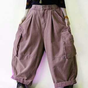 May include: Dusty rose, wide-leg cargo pants featuring a high-waisted design with a button closure, deep side pockets, and pleated detailing at the waist. The pants have a loose, voluminous silhouette with cuffed hems and visible stitching.