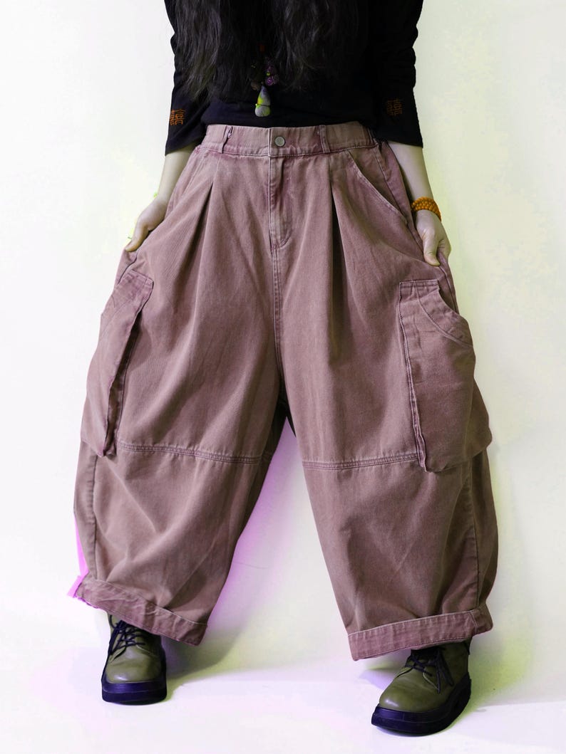 May include: Dusty rose, wide-leg cargo pants featuring a high-waisted design with a button closure, deep side pockets, and pleated detailing at the waist. The pants have a loose, voluminous silhouette with cuffed hems and visible stitching.