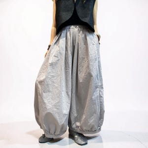 May include: Light gray wide-leg trousers featuring a voluminous, balloon-like silhouette with a gathered elastic waistband and a drawstring tie. The pants have a relaxed, loose fit that tapers slightly at the ankles with elasticized cuffs.