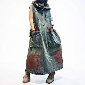 May include: A sleeveless, hooded denim maxi dress in a faded olive green wash. The dress features a button-up front, a drawstring hood, and multiple large patch pockets. Contrasting dark red, textured fabric panels are sewn onto the pockets and hem.