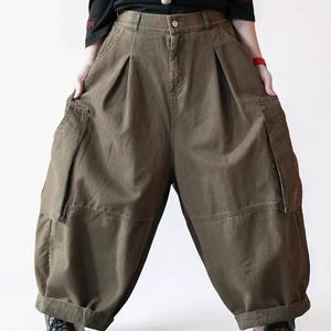 May include: Olive green high-waisted cargo pants featuring a wide-leg, loose-fitting silhouette, large side pockets, a button closure, and a cuffed hem. The pants are constructed from a durable fabric with visible stitching details along the seams.