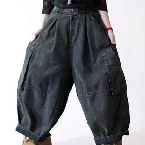 May include: Charcoal gray denim pants featuring a high-waisted design with front pleats, a button closure, and two large side cargo pockets. These wide-leg trousers have a relaxed, voluminous silhouette with cuffed hems and a faded wash finish.